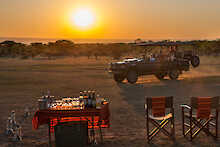 Ant´s Africa Safaris, Buschlandschaft, Sundowners auf gedecktem Tisch, Safarifahrzeug im Hintergrund