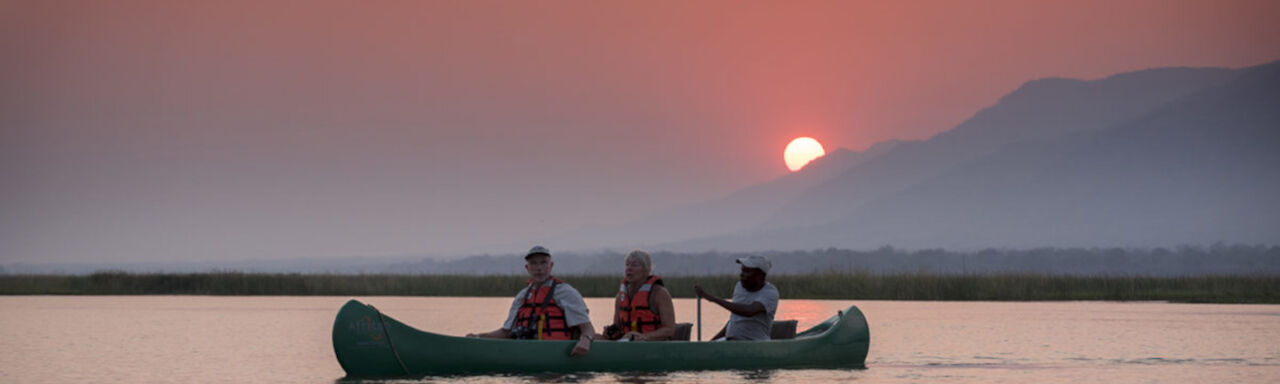 Gäste der African Bush Camps Zambesi Expeditions im Kanu beim Sonnenuntergang auf Zambezi-Fluss
