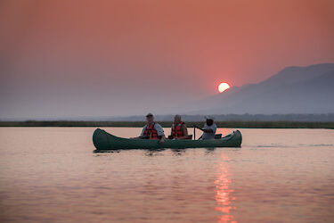 Gäste der African Bush Camps Zambesi Expeditions im Kanu beim Sonnenuntergang auf Zambezi-Fluss
