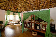 Schlafzimmereinrichtung mit Doppelbett und der Badewanne in der Arusha Safari Lodge