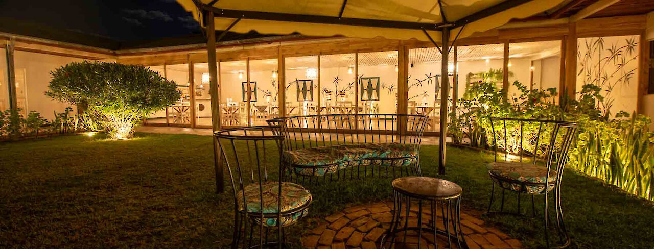 Tansania Mama Iringa Garten mit eleganter Sitzgruppe und Blick auf beleuchteten Restaurant mit Glasfront