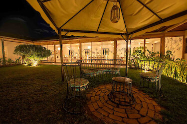 Tansania Mama Iringa Garten mit eleganter Sitzgruppe und Blick auf beleuchteten Restaurant mit Glasfront