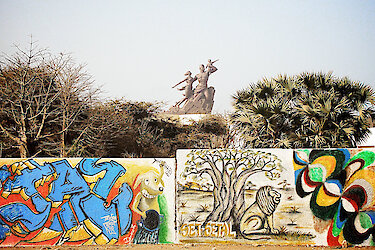 Bunte Mauer und im Hintergrund eine Statue von einem Mann, einer Frau und kleinem Kind