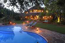 Ant´s Africa Safaris - Ant´s Nest, Pool mit Liegen und beleuchtetem Hauptgebäude im Hintergrund