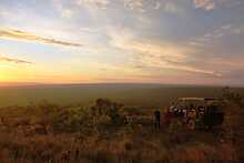 Ant´s Africa Safaris, Gäste mit Sundowners am Safarifahrzeug, Buschlandschaft im Hintergrund