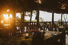 Vuma Hills Tented Camp Restaurant mit gedeckten Tischen und Sitzgelegenheiten, Sonnenuntergang im Hintergrund