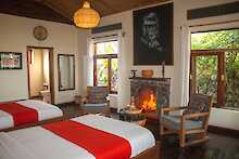Nkuringo Bwindi Gorilla Lodge Schlafzimmer mit zwei Einzelbetten und zwei Holzsesseln vor einem Kamin
