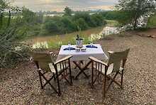 Campingstühle mit gedecktem Tisch und Blick auf Fluss und Natur