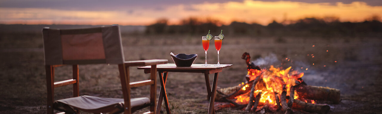 Ein Getränk bei Lagerfeuer und Sonnenuntergang im Tipilikwani Mara Camp